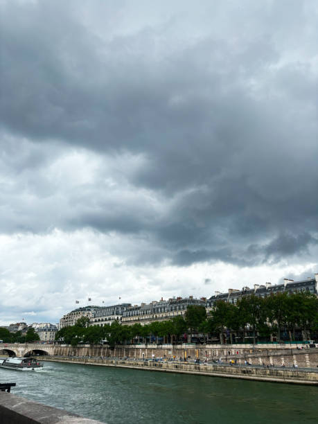 A cloudy day in Paris with a view of classic architecture along the river. The scene captures the calm ambiance of the city under a dramatic sky.