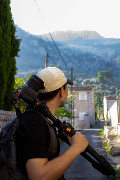 Adventurer holding tripod with camera on shoulder looking towards a mountain