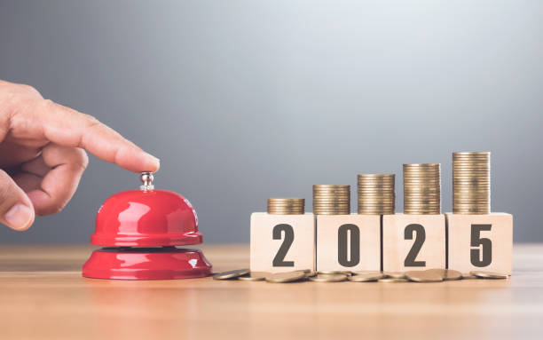 istock Hand presses a red bell next to a stack of coins on a wooden block labeled '2025,' representing financial goals and future planning with a sense of urgency for the upcoming year 2187092637