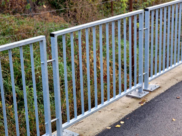 bridge railing with vertical fence posts anchored into the ground with four concrete screws. the railing is fixed from the side of the bridge into the concrete.