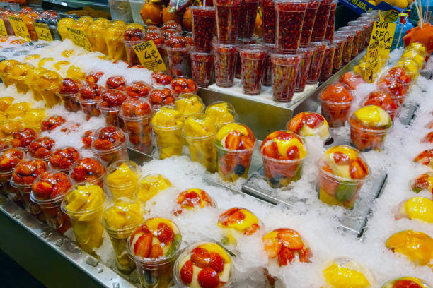 Barcelona, Spain, October 1, 2024: Vibrant display of fresh fruit cups filled with strawberries, oranges, and pomegranate seeds, chilling on ice in a bustling market stall. bright fruits are meticulously arranged, inviting customers to enjoy a refreshing treat.