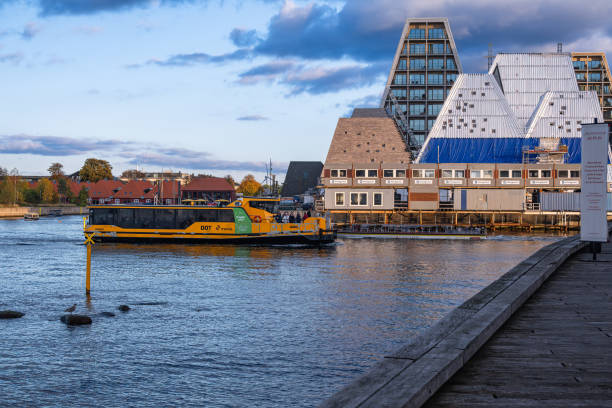 Copenhagen, Denmark - 6 October 2024: A vibrant yellow ferry navigates Copenhagen's serene waterway under a partly cloudy sky