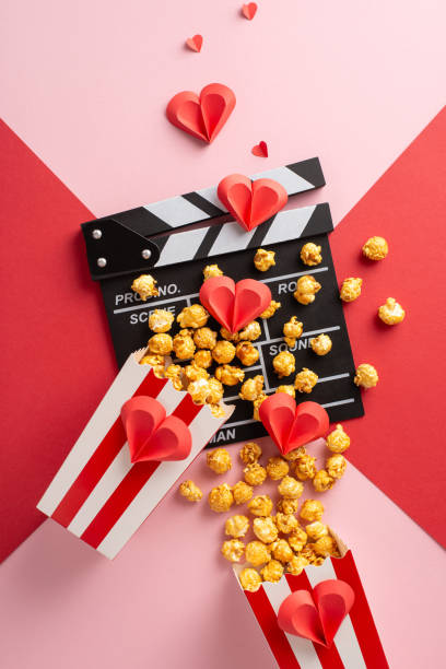 istock Popcorn vertical box and clapperboard arranged with paper hearts on a red and pink background, symbolizing romance and film 2187102006
