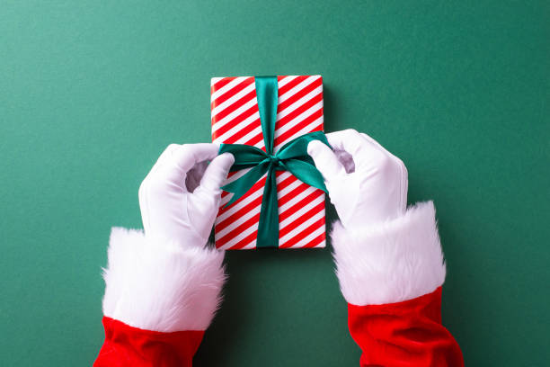 istock Santa Claus in white gloves packing a festive package adorned with a green bow over a bright green background capturing the holiday spirit 2187102019
