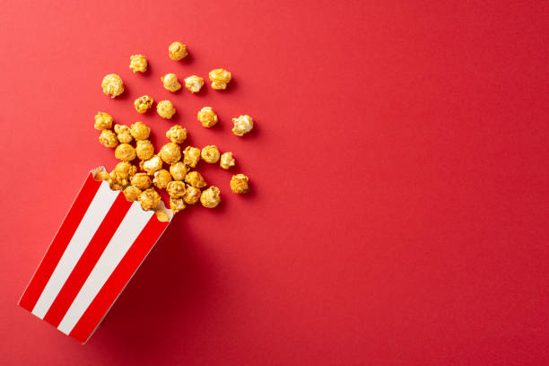istock Popcorn spills from a classic red and white striped box on a vibrant red background, creating a dynamic and eye-catching visual perfect for movie night themes 2187102024