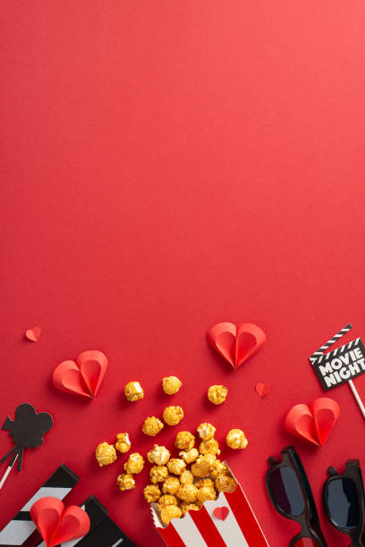 A vertical inviting setup for a romantic movie night on Valentine's Day featuring popcorn, paper hearts, and themed decorations on a red background