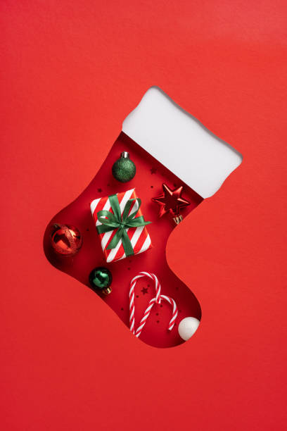 istock A vertical top view cut-out Christmas stocking filled with a wrapped gift, candy canes, and ornaments on a red background, perfect for the holiday season 2187102096
