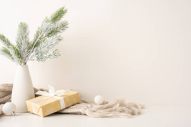 istock Minimalist side view Scandinavian style Christmas scene featuring a gift wrapped with ribbon, frosted pine branches in a vase, and cozy knit blanket 2187102162