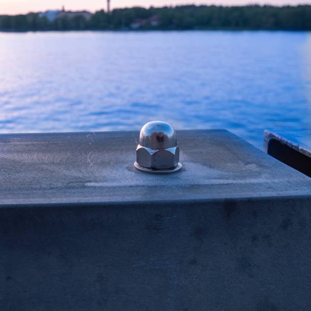 A giant screw and nut stand prominently by the tranquil sea, reflecting evening hues