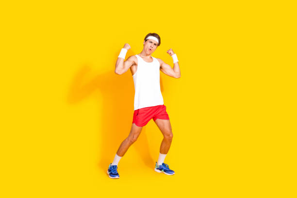 istock Energetic young man in activewear flexing muscles on vibrant yellow background, showcasing fitness and vitality 2187102663