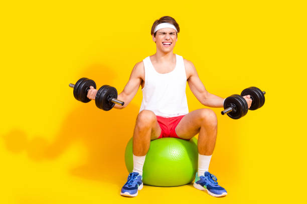 istock Young man lifting dumbbells in gym attire on a bright yellow backdrop 2187102683