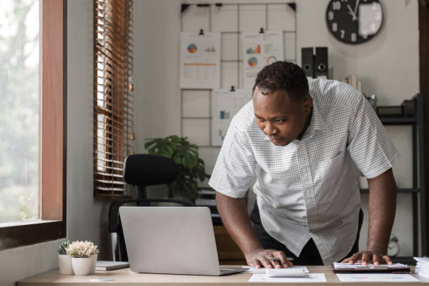 istock Stressed Male Office Worker Leaning Over Desk with Laptop in Modern Workspace 2187102916