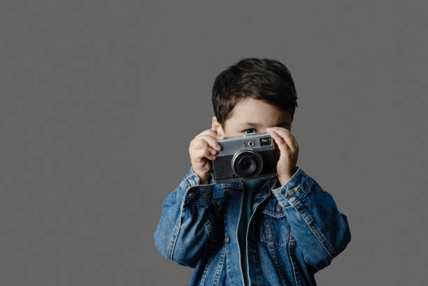 istock Cute little boy holding camera in hands and taking pictures 2187102950