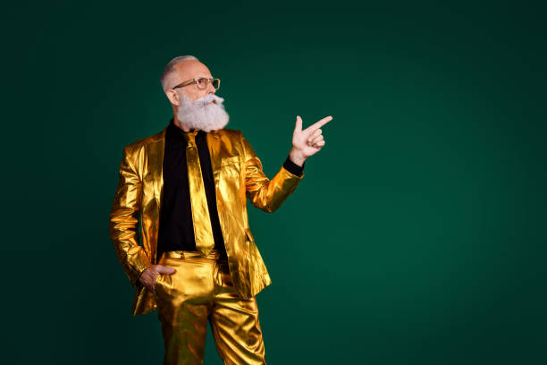 istock Charismatic elderly man in a golden suit pointing against a green backdrop symbolizing elegance and celebration 2187103425