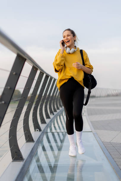 istock Cheerful woman strolls along a modern bridge, chatting on her phone while enjoying the serene cityscape at dusk by the water 2187103657