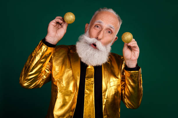 istock Elderly man in a golden suit celebrates with Christmas ornaments against a green background 2187103708