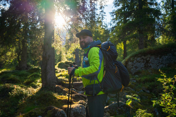istock Man Hiking in Sunlit Forest with Backpack and Hiking Poles 2187105202