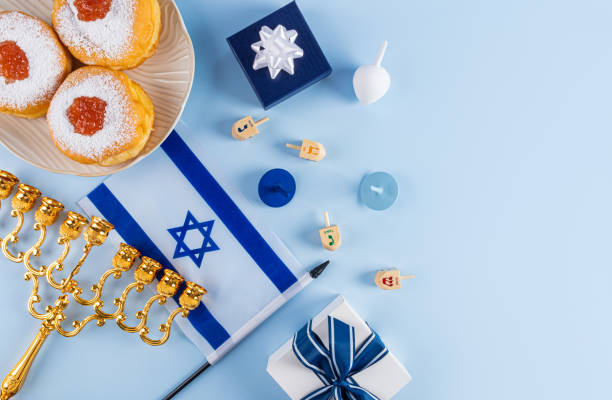 istock Fried donut with powdered sugar and jam on a plate, candles, minor, dreidels on a blue background. The concept of the Hanukkah. A copy space. 2187105995