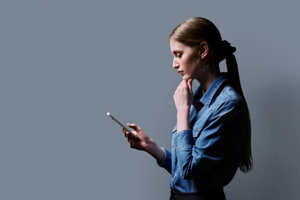 istock College student girl using smartphone, profile view, gray background 2187107271