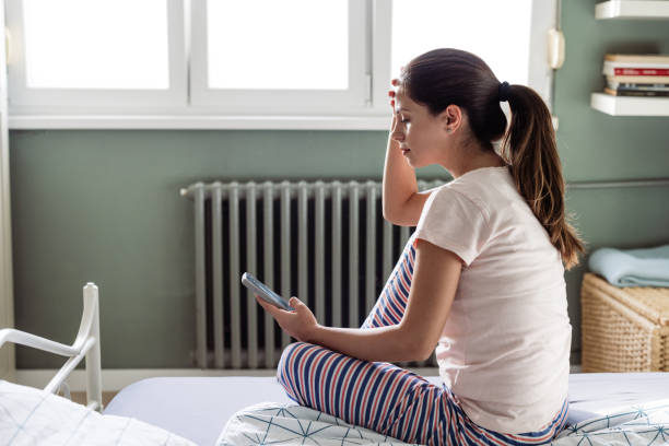 istock Young woman sitting on the bed and using phone 2187107545