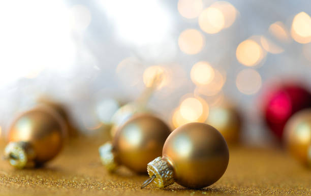 Close-up of golden Christmas baubles scattered against a sparkling bokeh background. The soft focus on the lights creates a warm, festive atmosphere, perfect for holiday-themed projects, greeting cards, and Christmas decorations.
