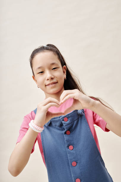 istock Smiling Asian Girl Showing Heart with Hands while Posing in Studio 2187109669