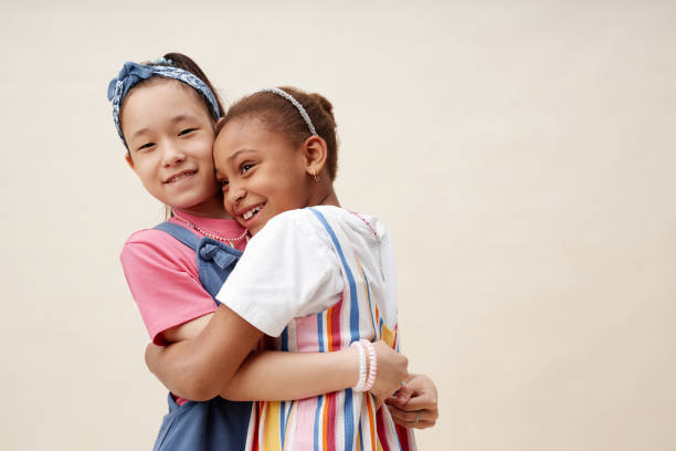 istock Smiling Asian Girl Hugging Female Friend while Having Fun on Neutral Background in Studio 2187109693