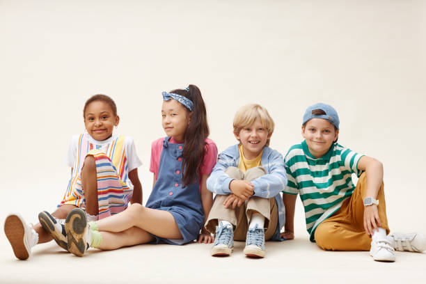 istock Smiling Kids in Colorful Clothes Sitting on Studio Floor against Neutral Background 2187109698