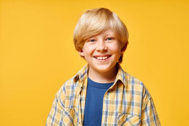 istock Blonde Smiling Boy in Plaid Shirt Standing on Yellow Background in Studio 2187109741
