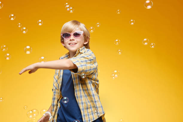 istock Little Boy Catching Soap Bubbles Floating around while Standing in Orange Studio 2187109756