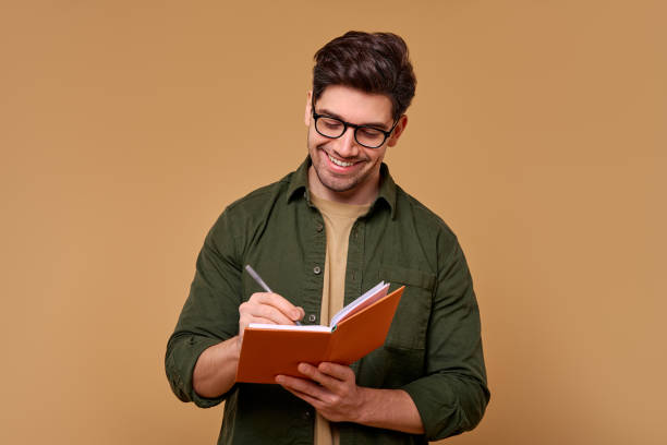 istock A Young Man Deep in Thought, Vividly Writing in His Notebook Against a Simple Background 2187112333