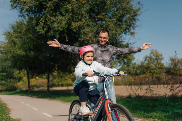 istock Father teaching daughter riding bicycle in park wearing helmet 2187112440