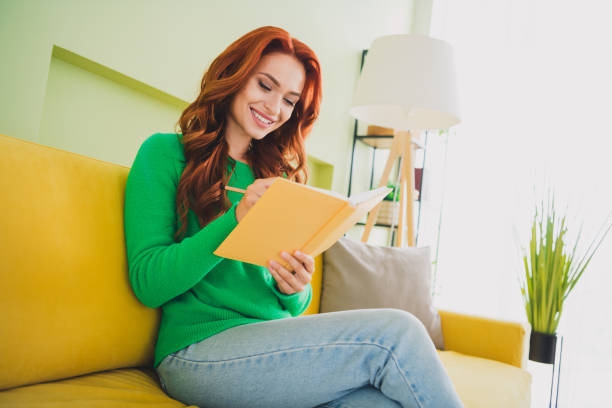 Photo of pretty young woman sit couch write notepad wear pullover weekend green interior apartment indoors.