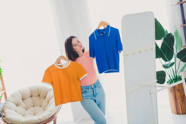 istock Charming young woman deciding between two colorful shirts in a cozy interior space 2187116141