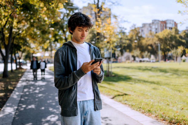 istock Young casually clothed man using smart phone while walking at sidewalk at public park 2187118494