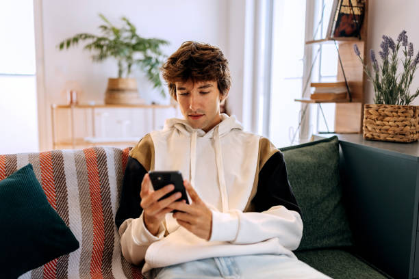 istock Casually clothed young man using smart phone while relaxing on a sofa at home 2187118834