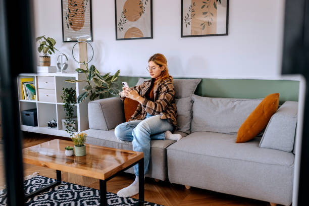 istock Casually clothed beautiful woman using smart phone while sitting on a sofa at home 2187118858