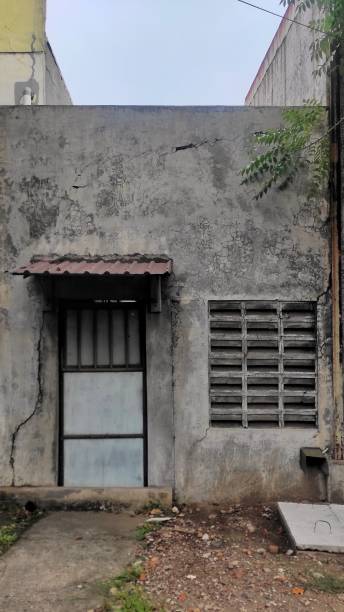 istock An aged, cracked wall featuring a backdoor with a small rusted roof and a ventilation grate, representing the rear view of an old warehouse structure. 2187120312