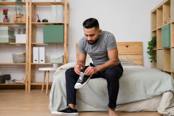 istock Young man tying shoelaces on bed in modern bedroom 2187120396