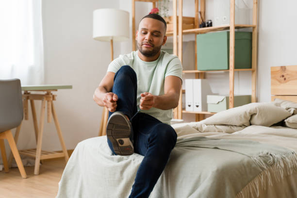 istock Young man tying shoelaces while sitting on bed in bedroom 2187120758
