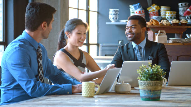 istock Three Businesspeople Sitting At Table Working At Laptops In Coffee Shop 2187120770