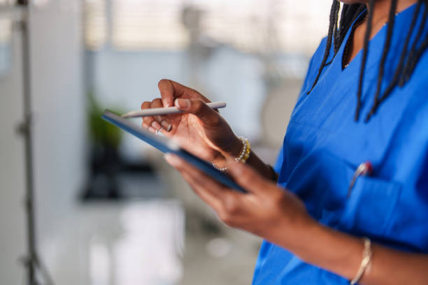 Close up to healthcare worker with blue scrubs hands using digital tablet.