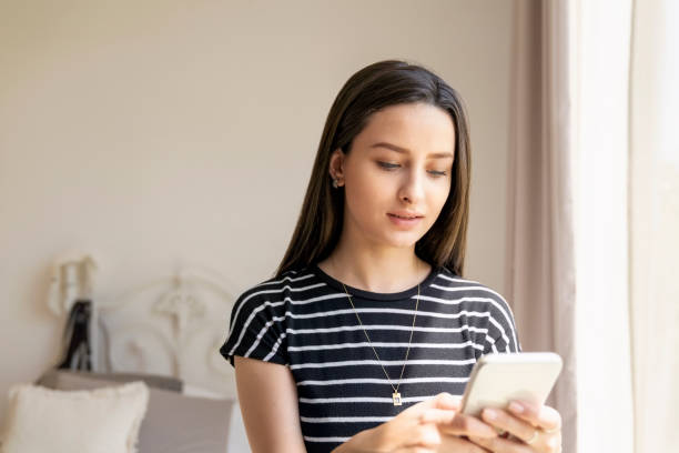 istock Young woman reading text message on her mobile phone at home 2187124984