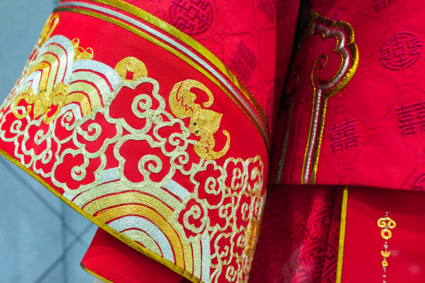 The image highlights a section of a traditional Chinese bridal attire, exquisitely embroidered with gold on a rich red fabric. The embroidery features auspicious motifs such as a dragon, which is a symbol of power and good fortune in Chinese culture, and is often associated with imperial dignity and strength. The intricate patterns are bordered by a fine gold trim, adding to the garment's regal appearance. The character \