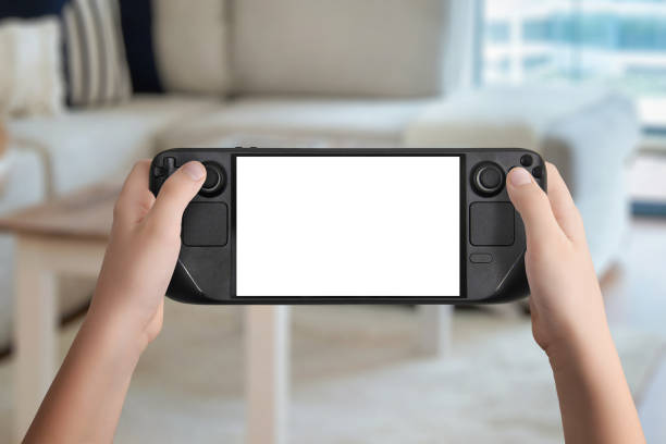 istock Flat lay or front view of hands holding a black handheld gaming console with isolated screen, cozy living room background, ideal for mockup game presentation and design 2187127820