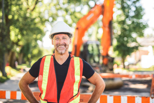 caucasian engineer with white helmet at work and having a mechanical shovel on the back stock photo