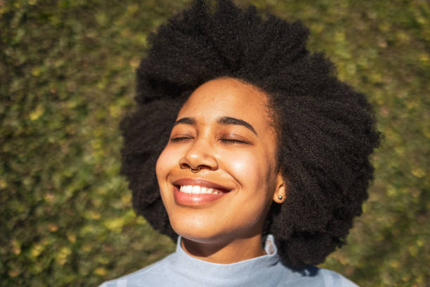 Portrait of a smiling Latin woman contemplating/ breathing. . She is wearing light blue shirt on a green leafy background