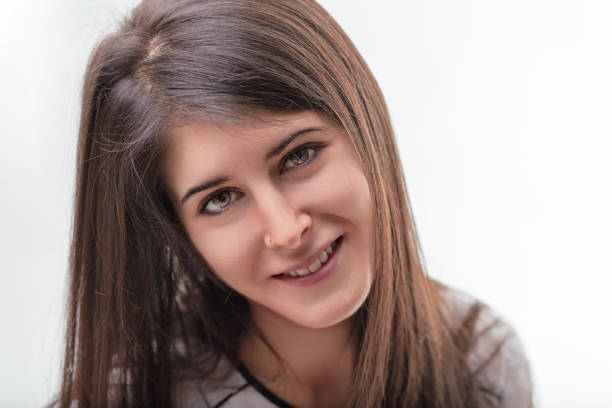 Young woman smiles confidently, radiating happiness and joy, looking directly at the camera against a clean white background