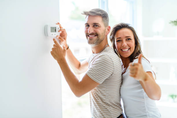 istock Smiling couple Adjusting Thermostat On Home Heating System 2187142934