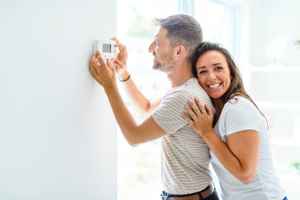 istock Smiling couple Adjusting Thermostat On Home Heating System 2187142939